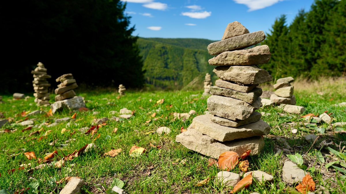 Serene mountain scene with creatively stacked stones in a lush meadow under a clear blue sky.