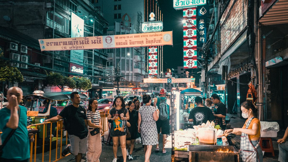 Explore the vibrant street market in an Asian city at night filled with people and neon lights.