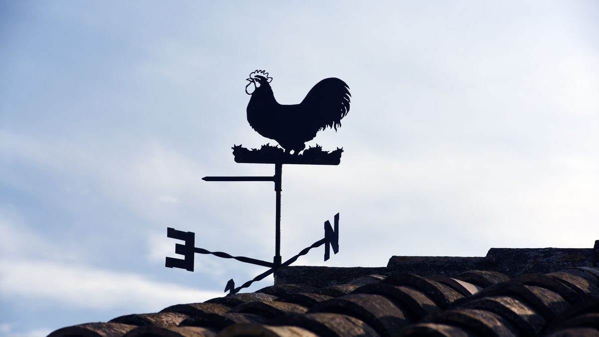 Silhouette of a rooster weather vane on a rooftop against a clear sky, direction indicator.