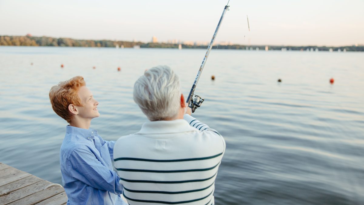 A grandfather and grandson enjoying a peaceful fishing trip on a dock by the ocean.