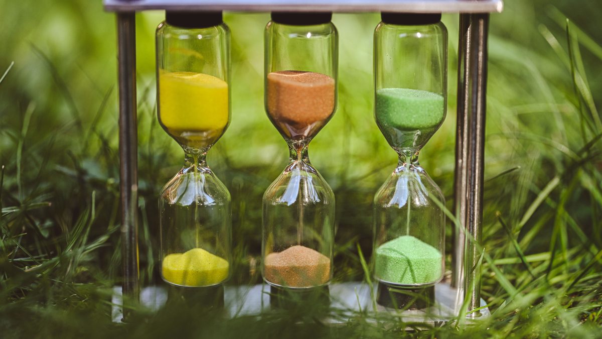 A vibrant triple hourglass with yellow, orange, and green sand set in a lush grassy meadow.