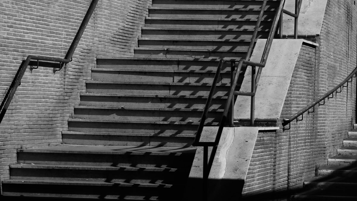 Black and white photograph of a flight of worn stone steps rising between walls on a narrow city street.