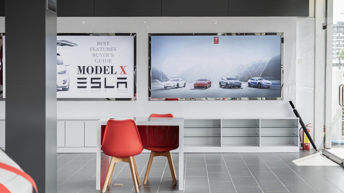 Spacious car dealership interior featuring red chairs and advertising displays with electric cars.