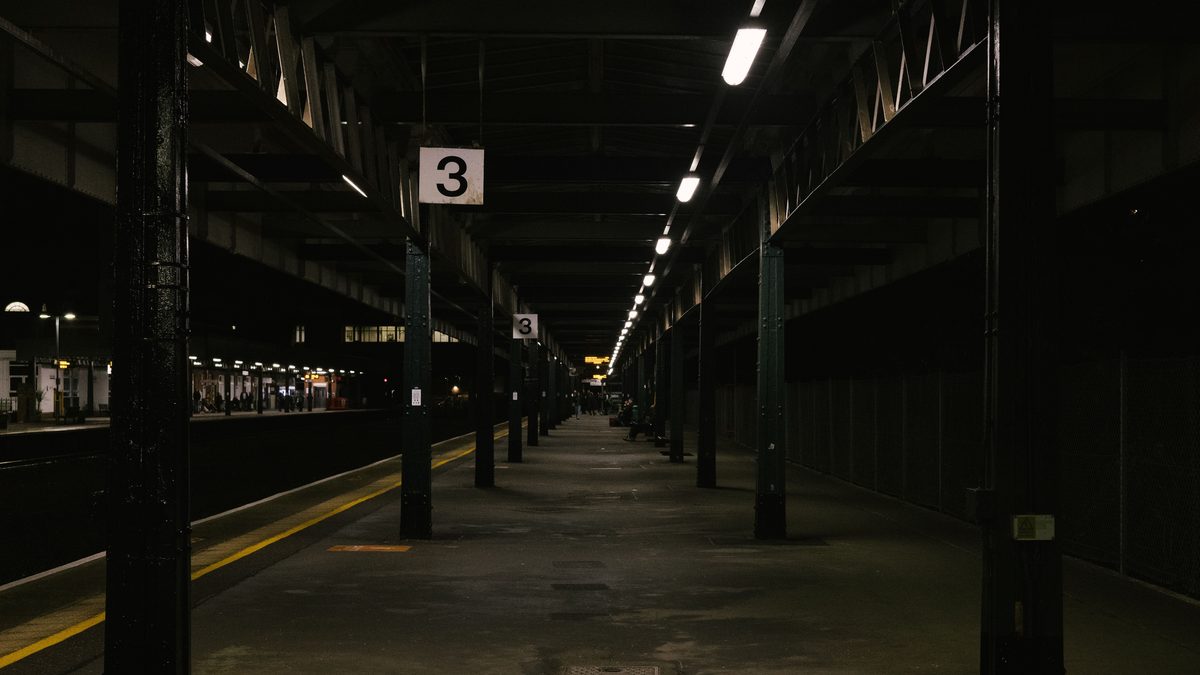A dimly lit, moody railway station platform at night, conveying urban solitude.