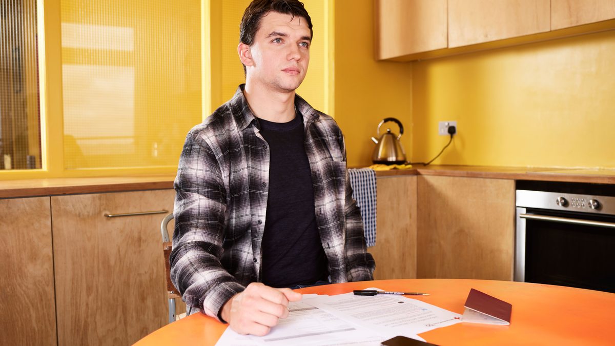 Adult man sitting at kitchen table reviewing documents with focus and concentration.