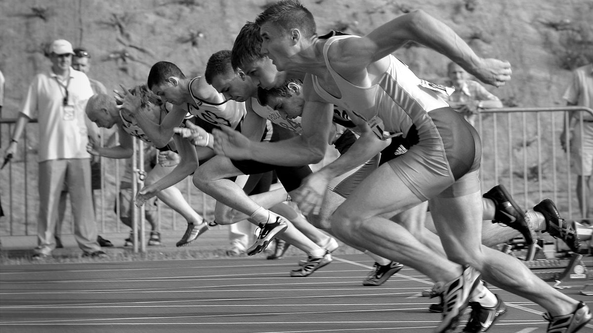 Athletes burst from the blocks during a sprint race, captured in monochrome.
