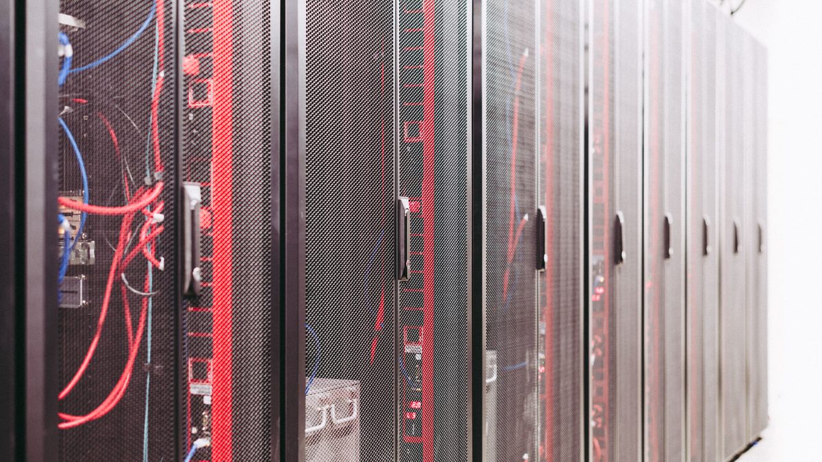 A row of black mesh-fronted server cabinets in a data centre aisle, with red and blue patch cables visible through the door of the nearest rack.