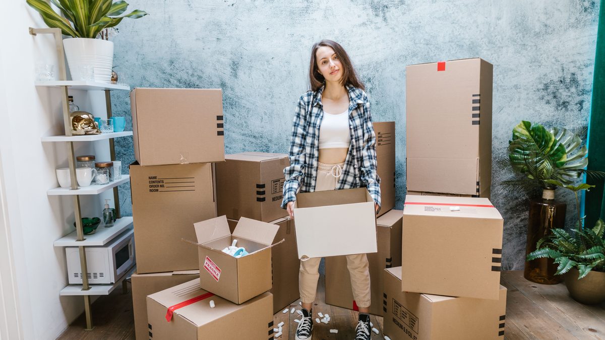 A woman organizing cardboard boxes filled with packing materials in a sunlit living room, preparing for a move.