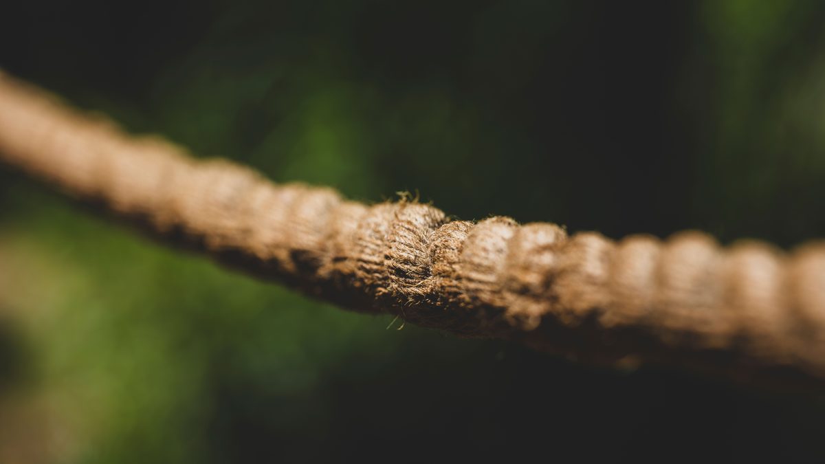 Macro shot of a frayed, weathered nautical rope against a green, blurred background.