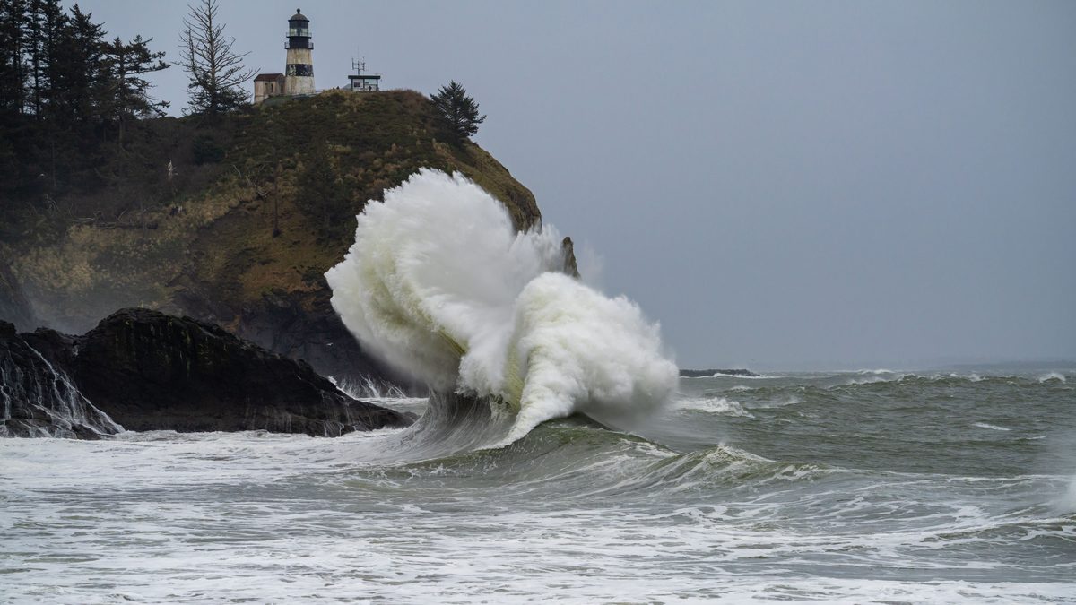 Dramatic ocean waves crashing against a scenic cliffside lighthouse, capturing nature's raw power.