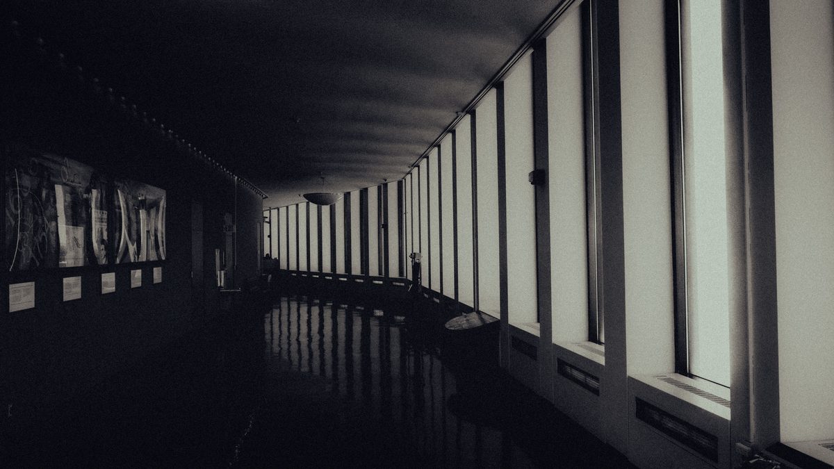 A moody, dimly lit corridor with large windows and abstract artwork on the walls.