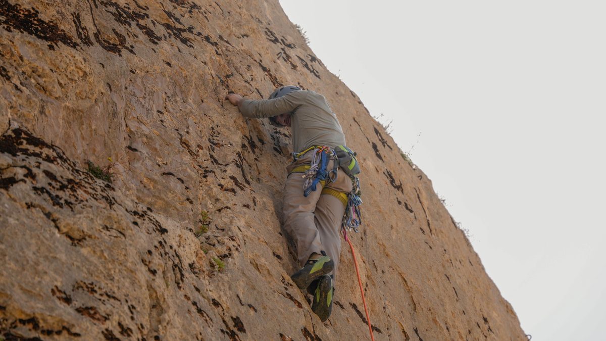 A focused rock climber scaling a limestone cliff with climbing gear in Damascus, Syria.