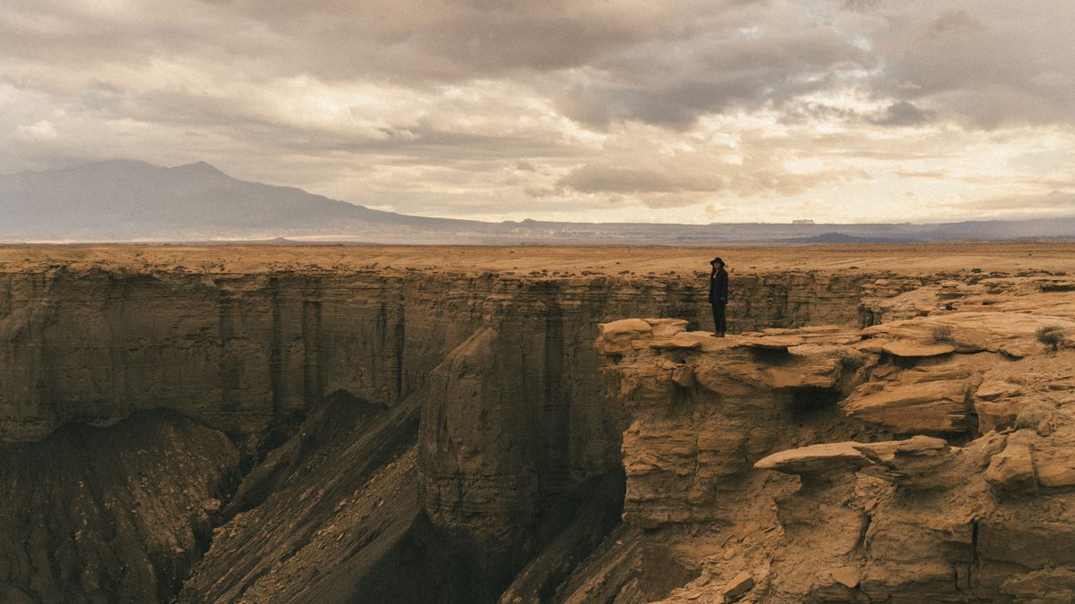 Woman stands on edge of rocky canyon in Utah. Dramatic landscape and cloudy sky.