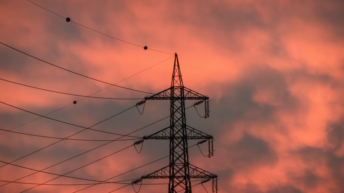 A striking silhouette of an electricity pylon against a vibrant sunset sky.