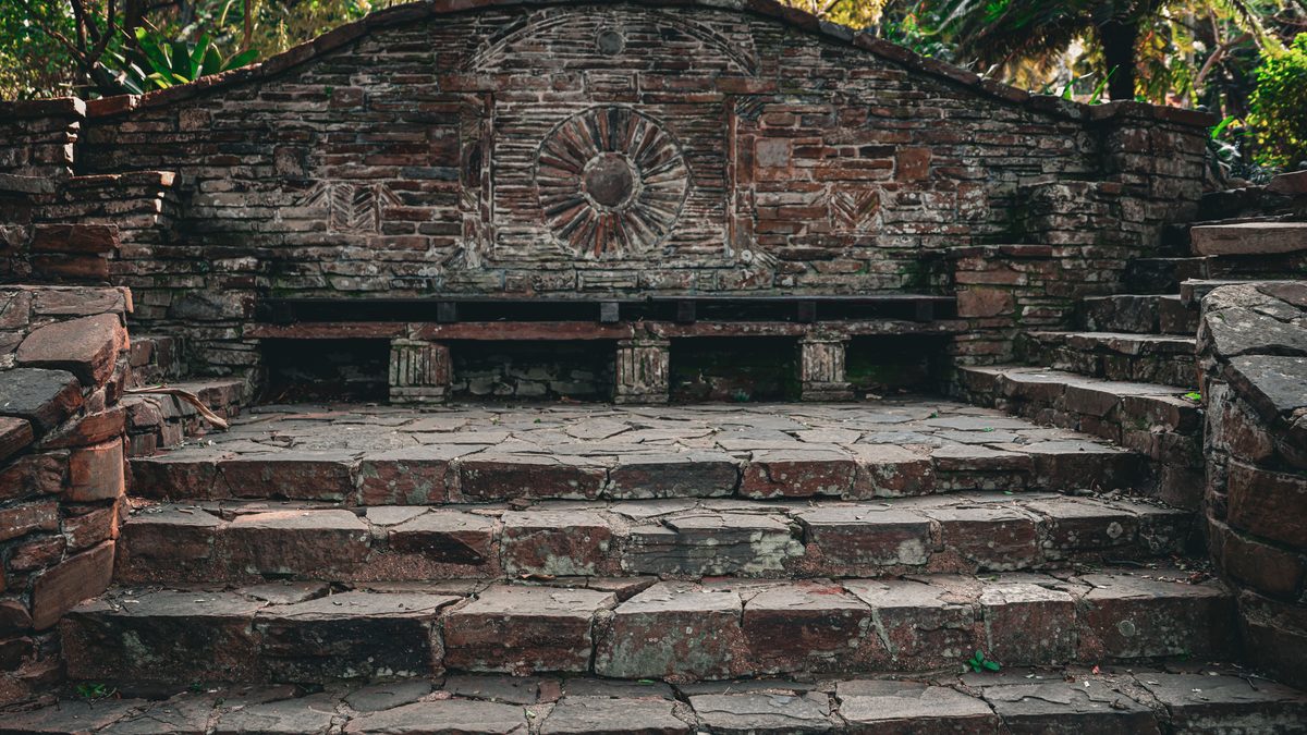 Four broad flights of weathered flagstone steps rising to a curved brick garden bench carved with a sunburst, the stone cracked and lichen stained.