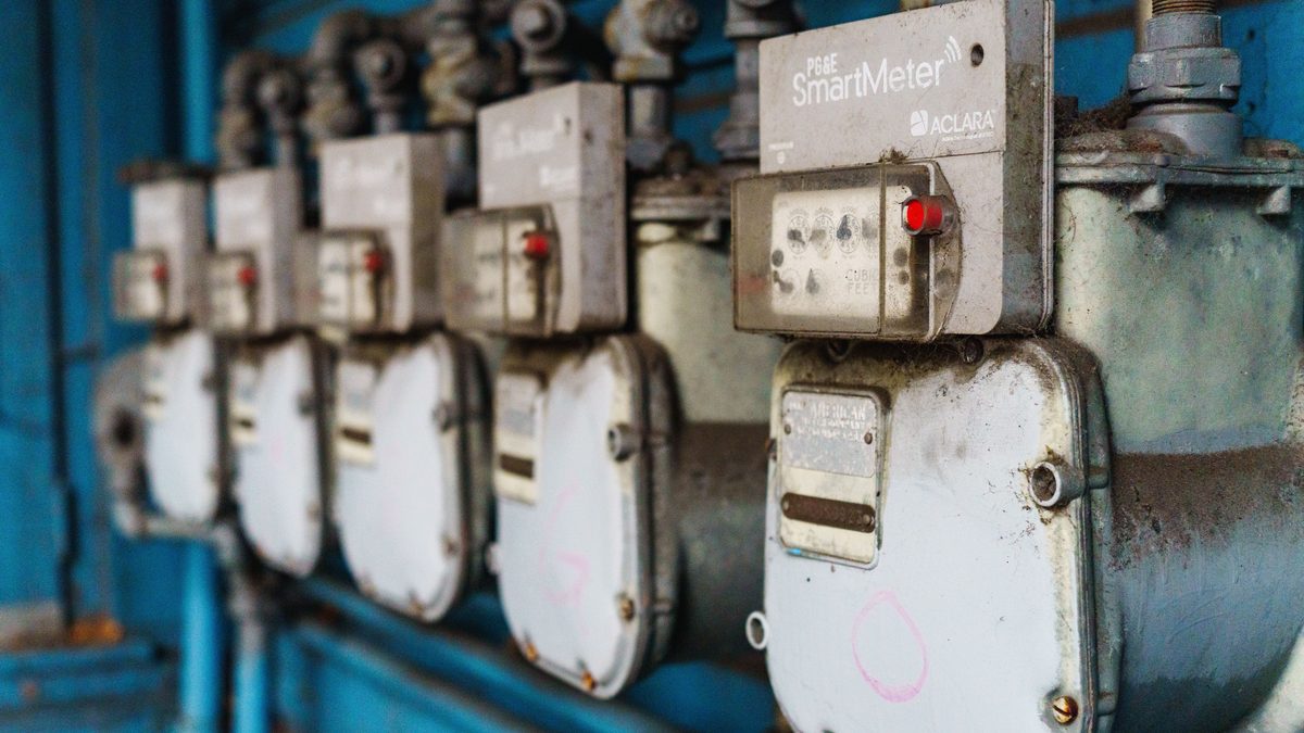 Multiple smart utility meters lined up on a blue industrial wall.