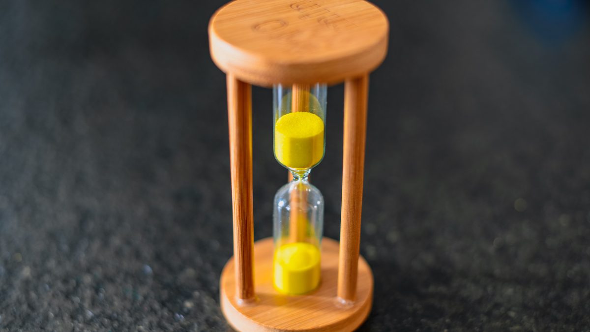 Close-up of a wooden hourglass with yellow sand on a dark textured surface.