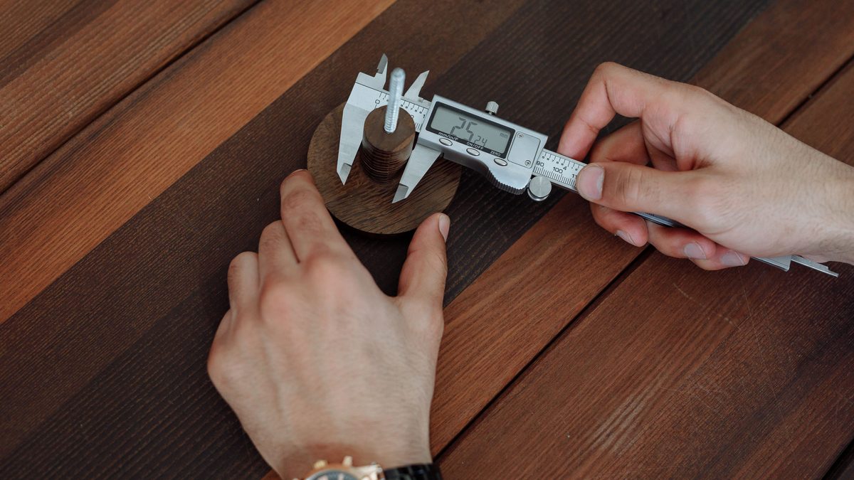 Detailed view of hands using a digital caliper on a wooden table.