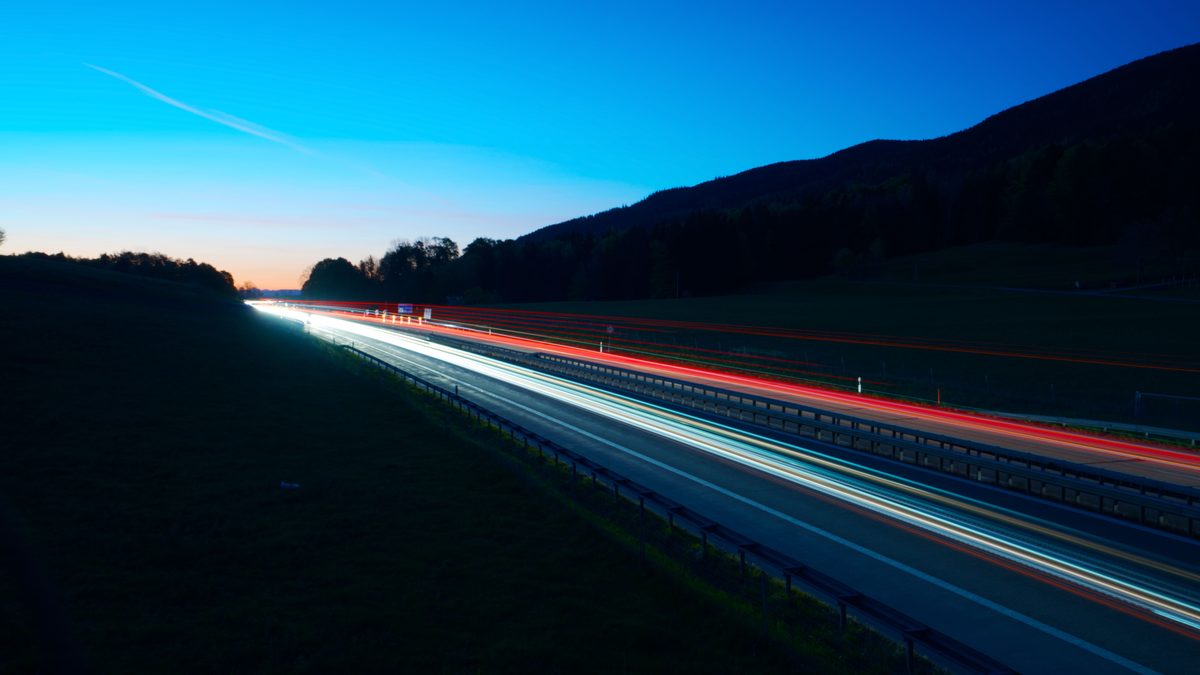 Vivid long exposure of highway lights during twilight with clear sky backdrop.