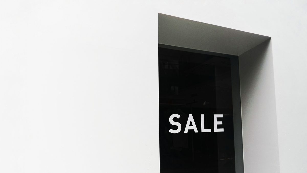 A minimalist black and white image of a sale sign on a store window with ample negative space.