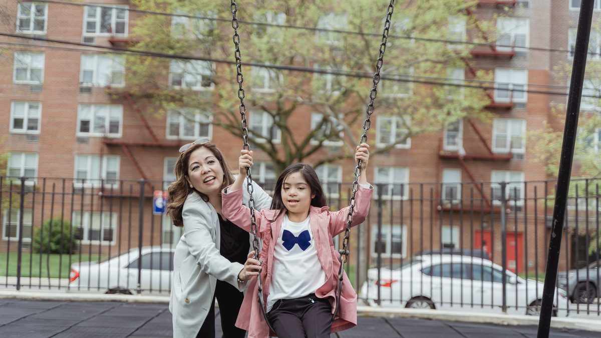 Mother and daughter having fun on a swing set in a city playground.