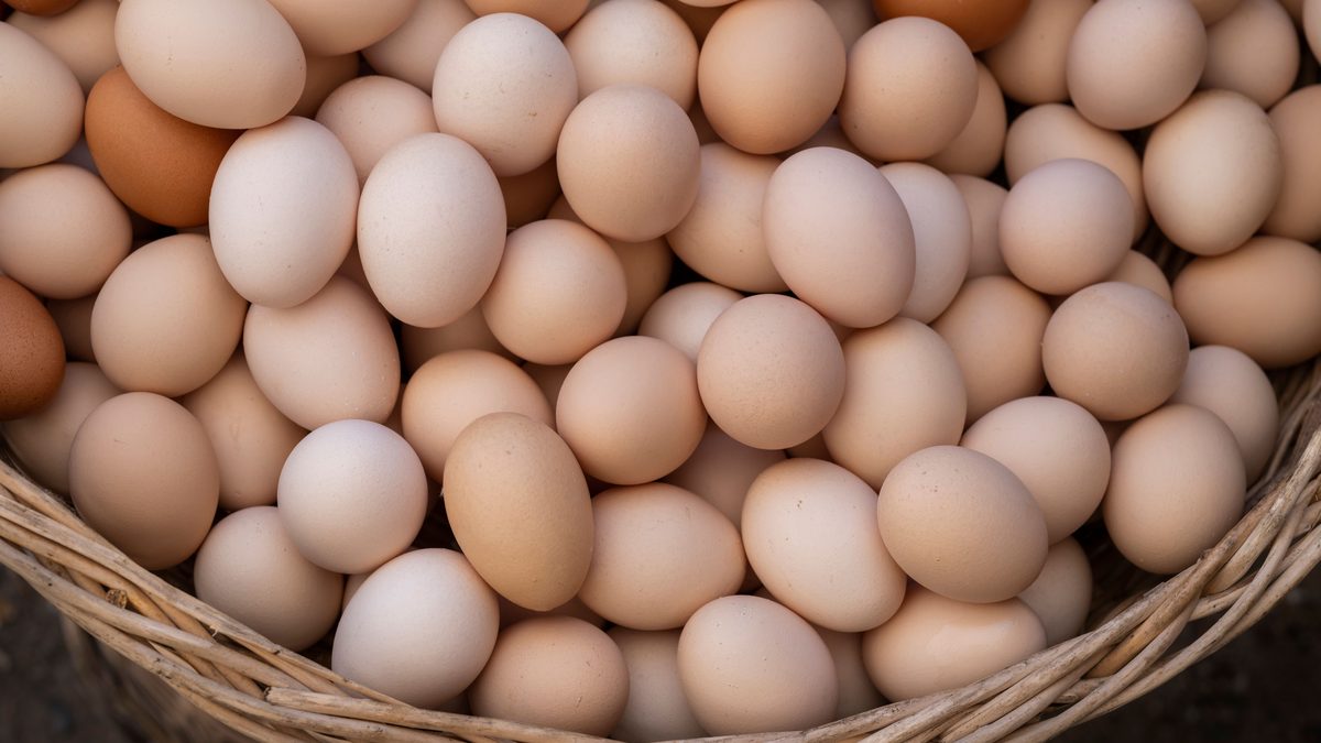 A heap of fresh brown and white eggs in a wicker basket, captured from above.