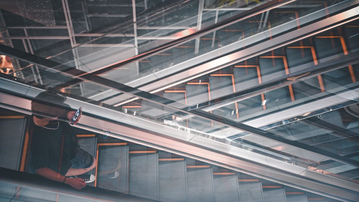 A man using his phone on modern escalators with architectural reflections.