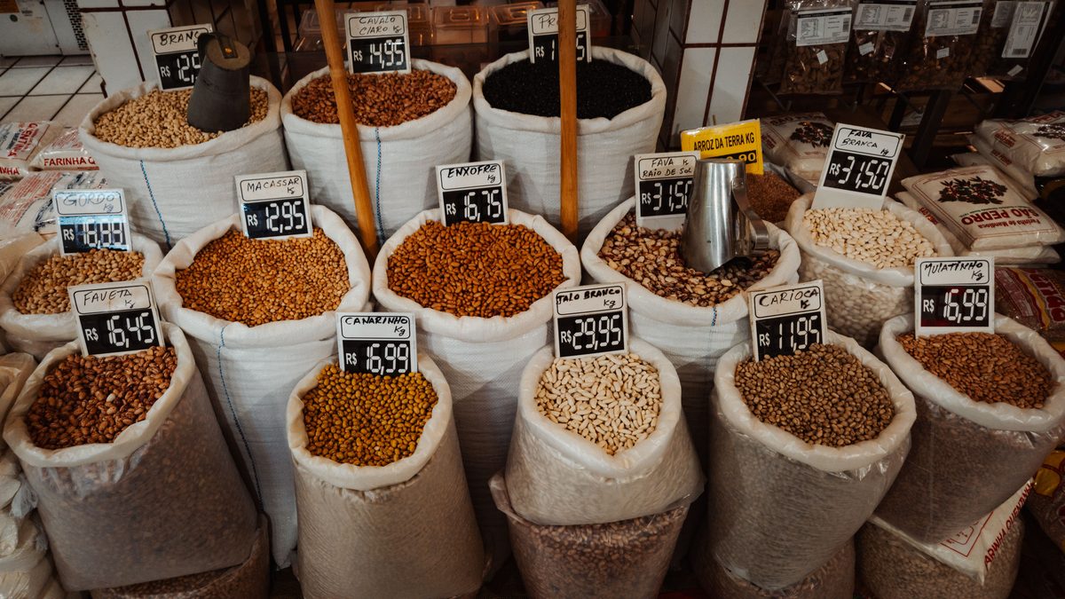 Colorful market display of various beans in large sacks with price tags.