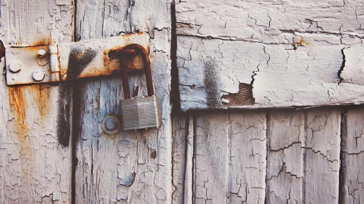 Close-up of a rusty padlock on a textured vintage wooden door with peeling paint.