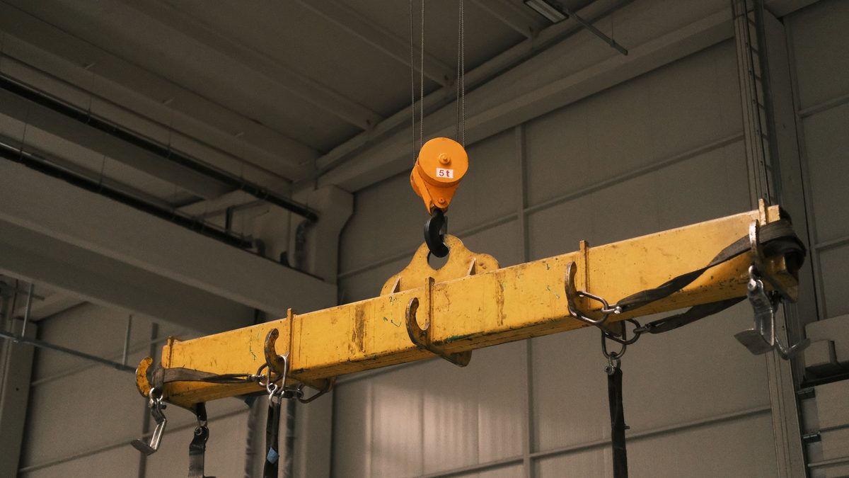 Close-up of a yellow industrial crane hoist, its steel cable and hook drum bearing a load.
