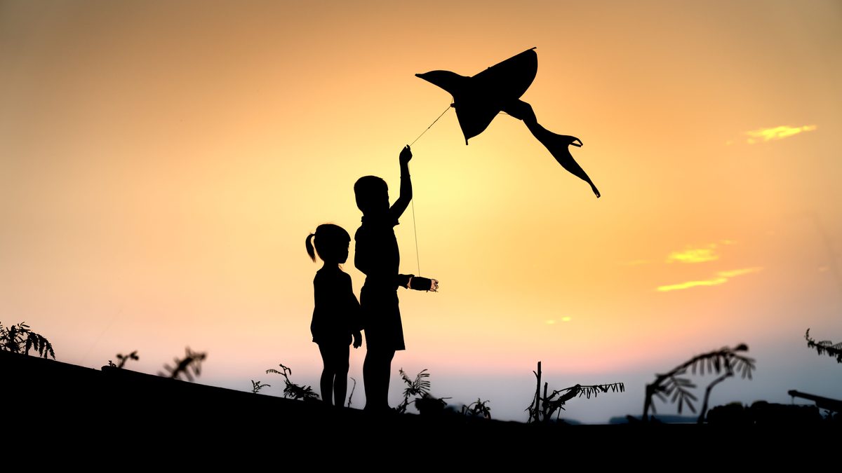 Two children flying a kite at sunset, captured in a scenic silhouette.