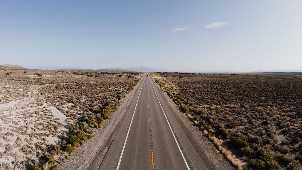 Aerial view of an empty desert road stretching into the horizon under a clear blue sky.