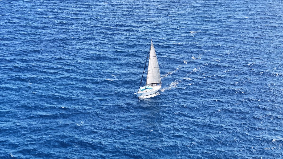A lone sailboat gliding over deep blue waters off the coast of Spain in the Mediterranean Sea.