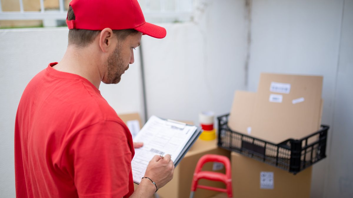 Delivery person in red uniform checks packages. Outdoor location, Portugal.