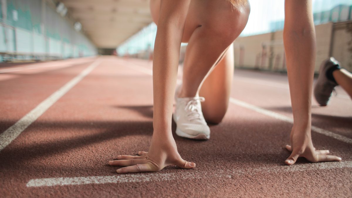Faceless female sprinter in running crouch start pose putting hands on starting line on track.