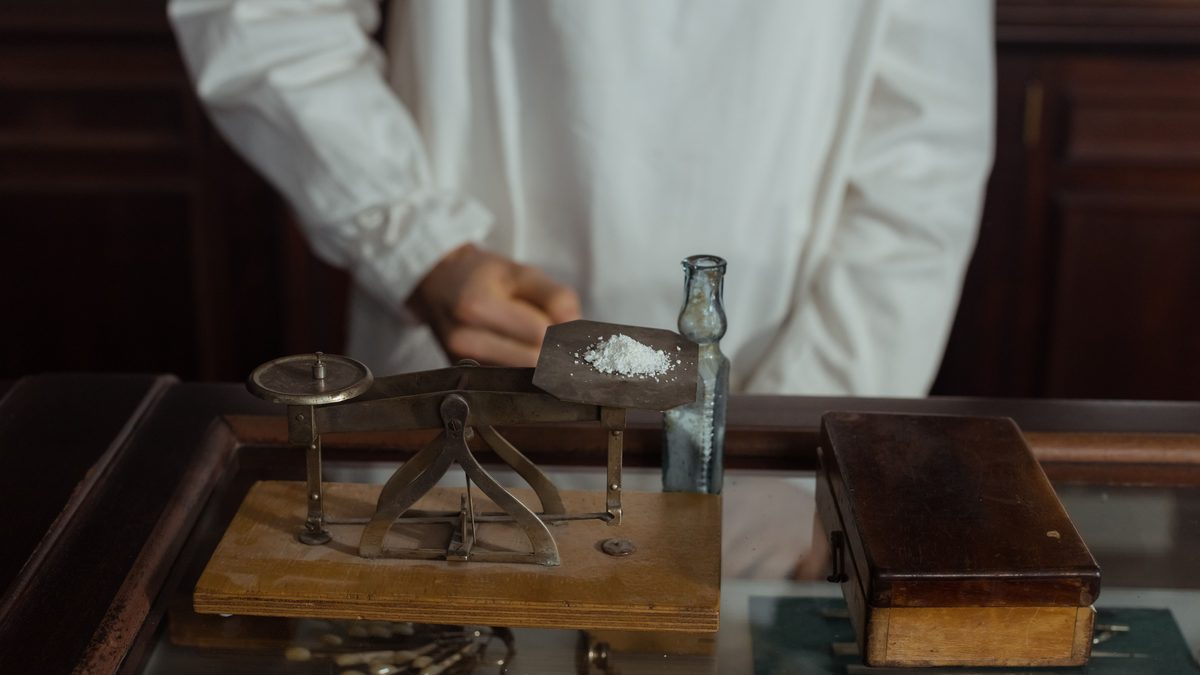 A pharmacist in a white gown working with a vintage scale and medicine bottle, showcasing retro pharmacology tools.