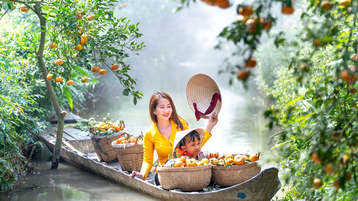 Asian mother and child harvesting oranges from a boat in lush orchard.