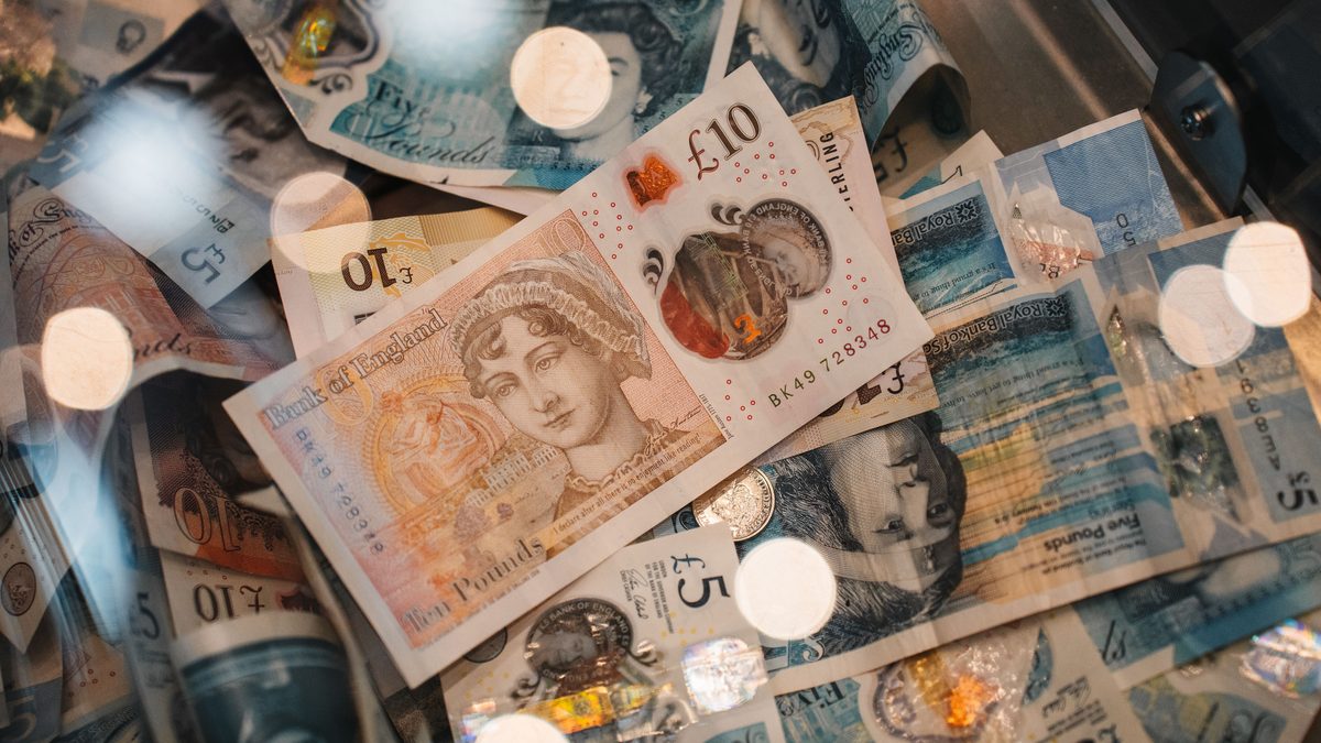 Scattered Bank of England ten pound and five pound notes photographed from above with a few coins, lit by warm bokeh highlights.