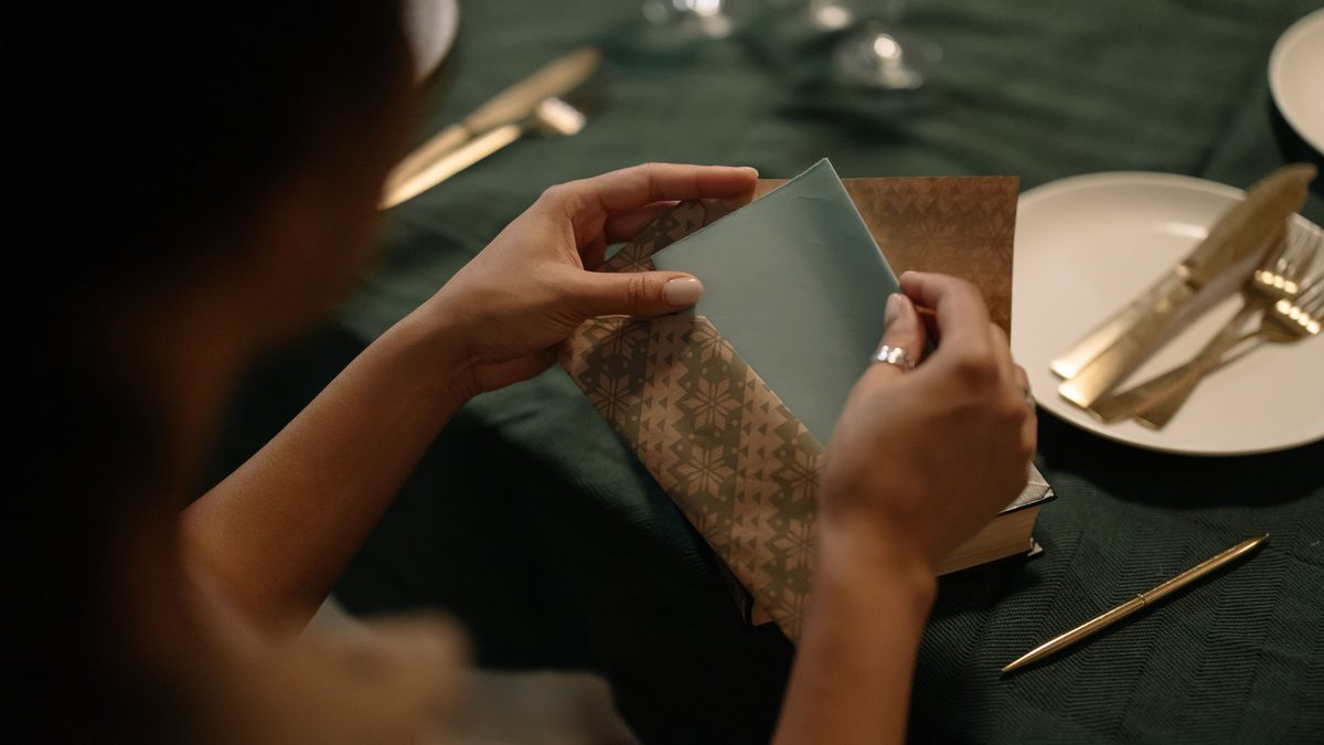 A close-up view of a woman inserting a letter into an envelope on a dining table.