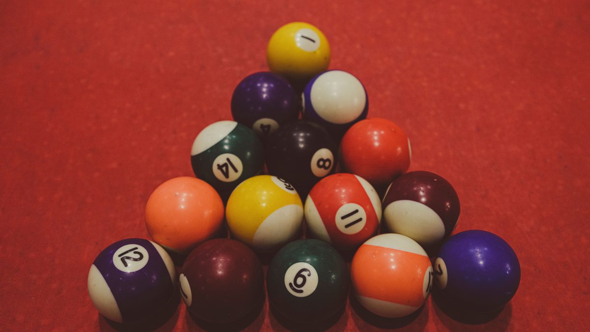 Numbered billiard balls racked in a tight triangle on a red cloth table, photographed close up under warm light.