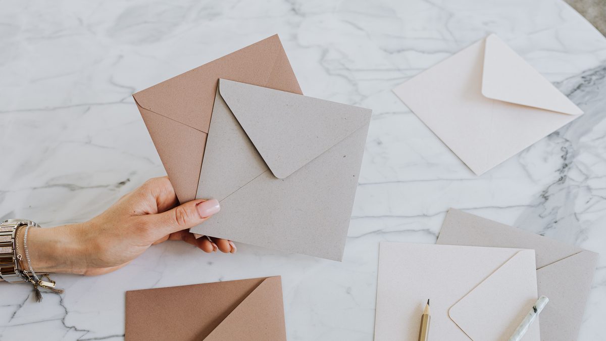 A hand holding craft envelopes on a stylish marble table with pencils, showcasing an artistic layout.