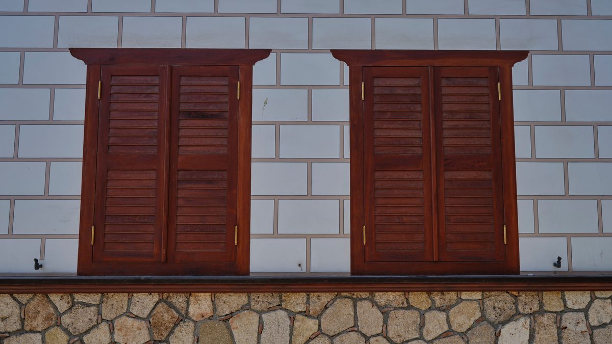A close-up of vintage wooden shutters against a stone and brick wall.