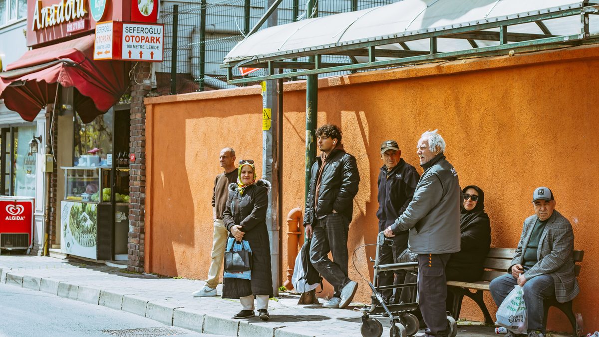 A diverse group of people waiting at a bus stop in an urban setting during the day.