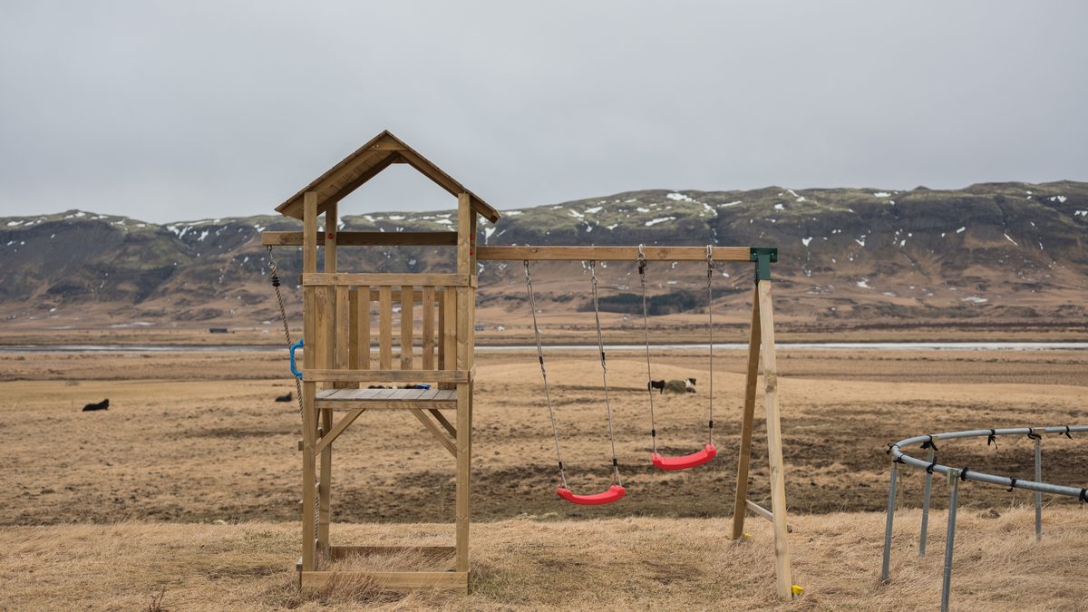 A wooden playground set overlooking a serene landscape with mountains and open fields under a cloudy sky.