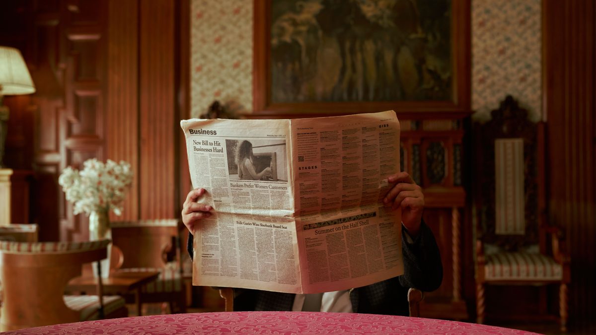 Person reading a newspaper in a luxurious, old-fashioned interior.