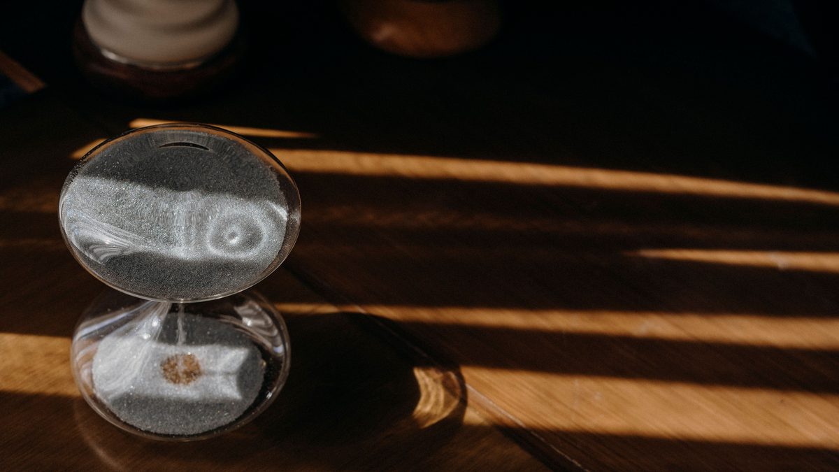 Peaceful sand timer casting shadows on a wooden table in warm morning sunlight.