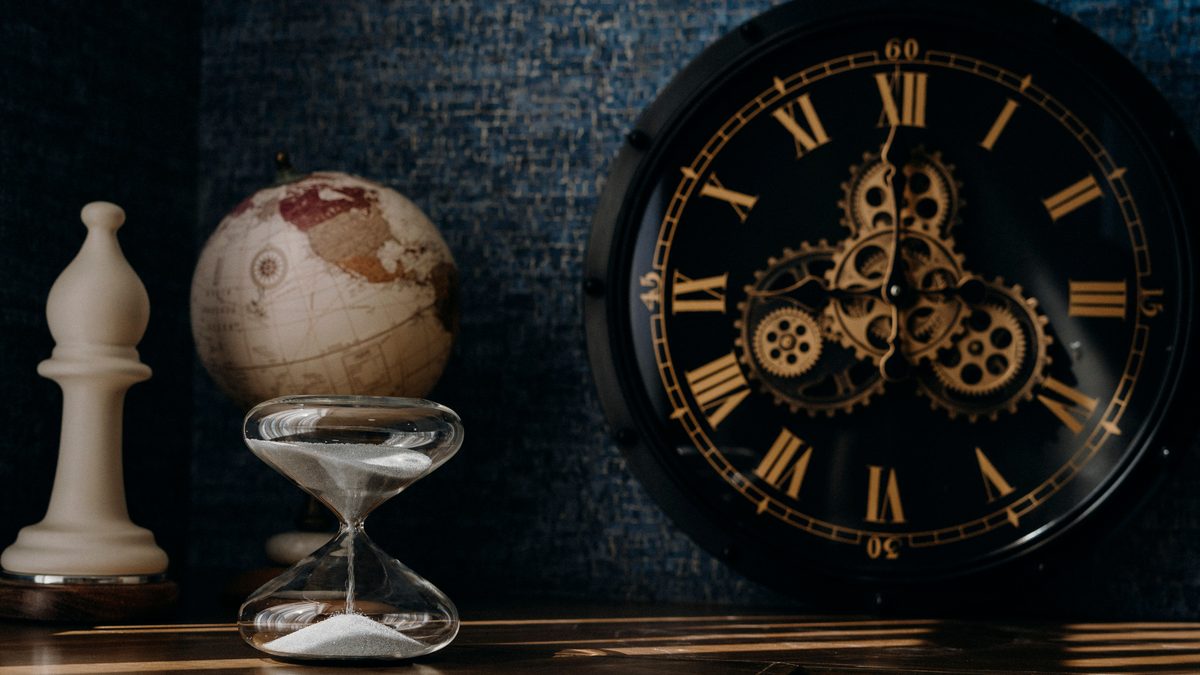 A dark and moody still life featuring an ornate clock, globe, and hourglass.