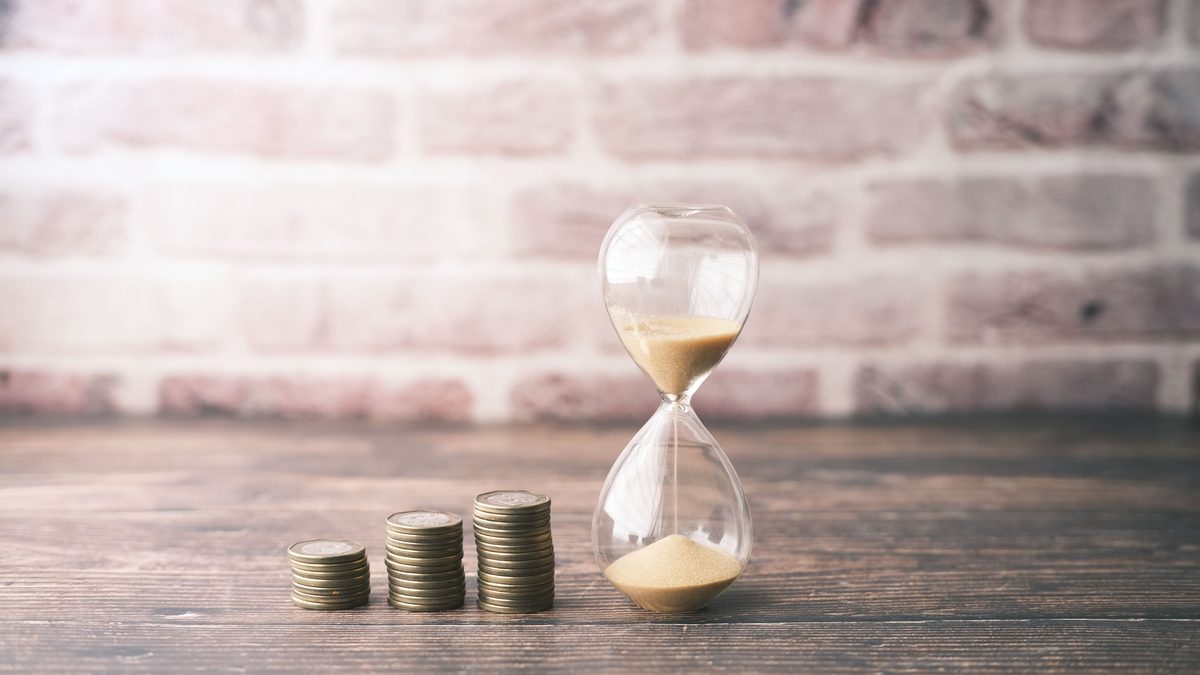 Hourglass and stacked coins on wood, symbolizing the concept of time and money.