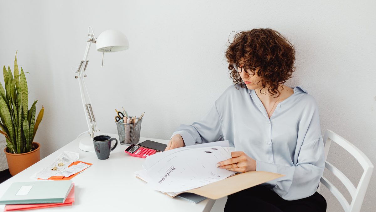 Woman reviewing documents in home office with plant and lamp.