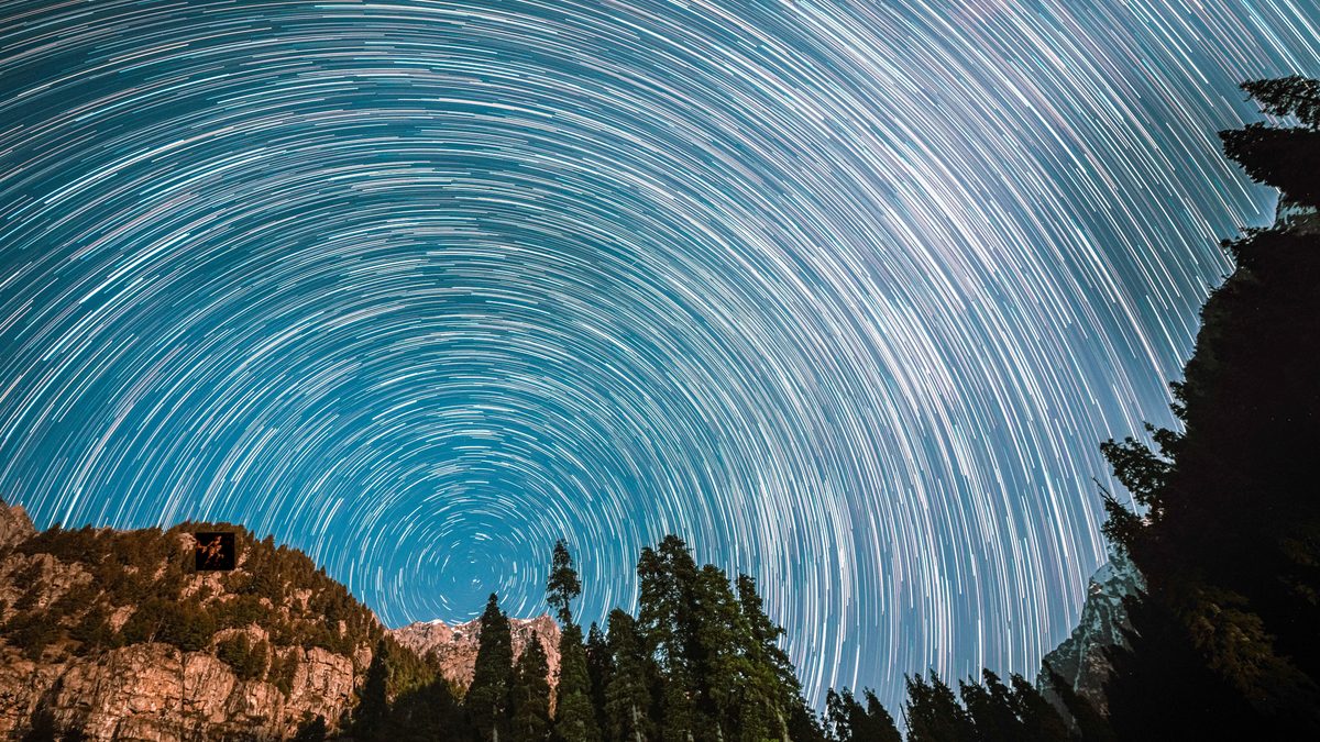 Long exposure capturing mesmerizing star trails above forested mountains at night.